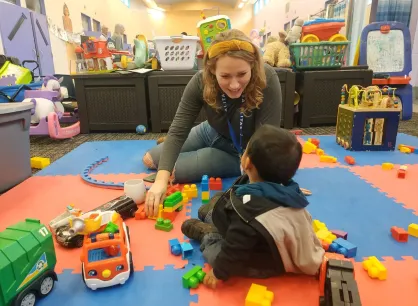 Une personne souriante est assise par terre avec un petit enfant.